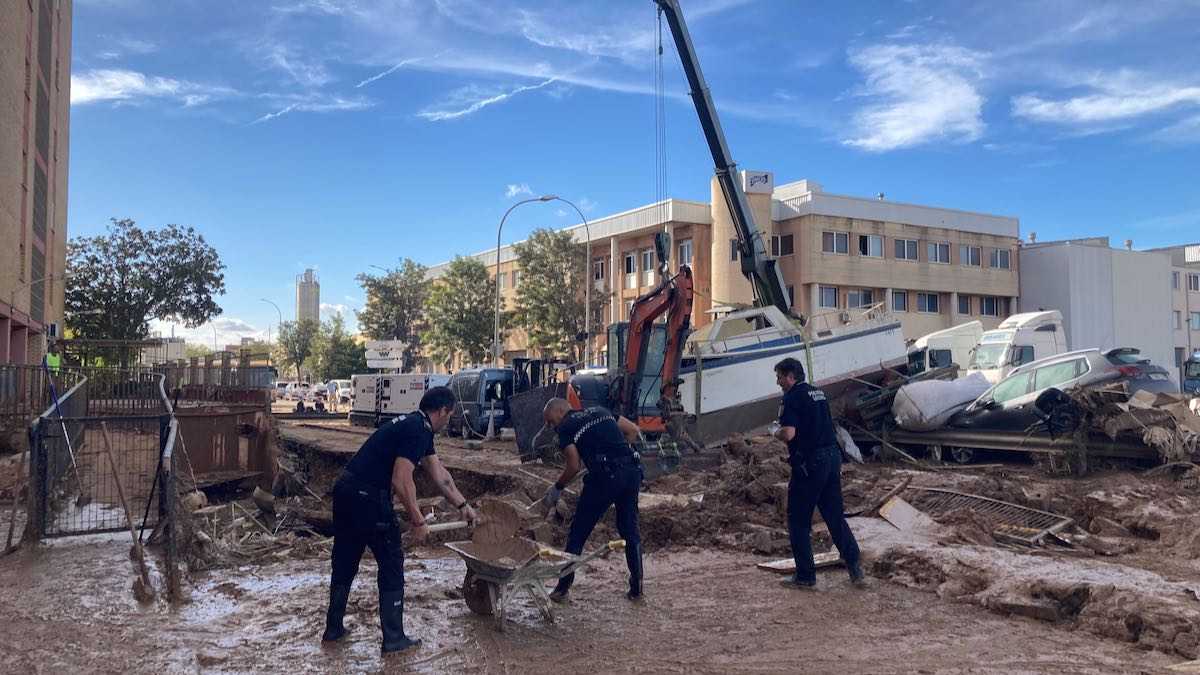 Police help to shovel mud away after flash floods from the 2024 DANA. In the background a crane is trying remove cars piled up from the floods.
