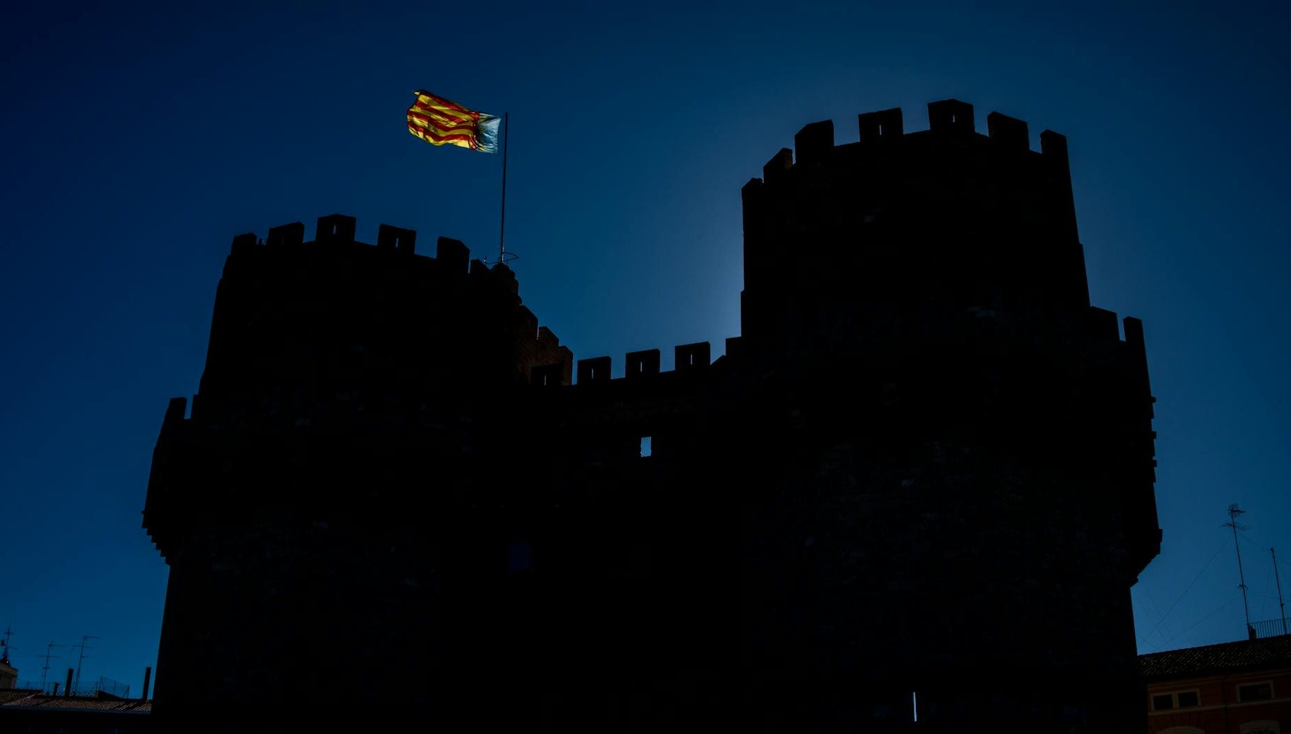 The silhouette of Valencia's iconic Torres de Serranos with a blue, yellow and red Valencian flag flying