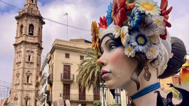 Fallas ninot of a woman's head with colorful headdress near the Micalet bell tower in Valencia