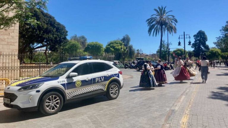 A police car parked next to Torres Serranos as women in traditional Valencian dress walk by
