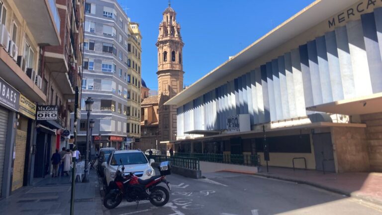 Street view of the white slats on Ruzafa Market with church bell tower in the background.