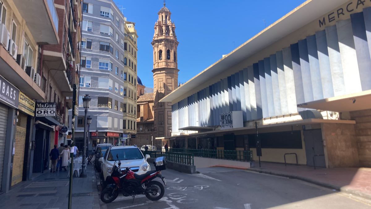 Street view of the white slats on Ruzafa Market with church bell tower in the background.