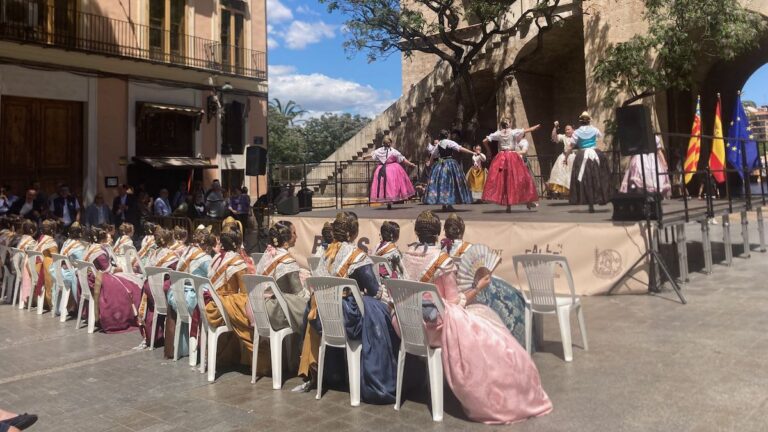 A row of women in traditional Valencian dress watching traditional dancing on a stage in front of Torres Serranos.