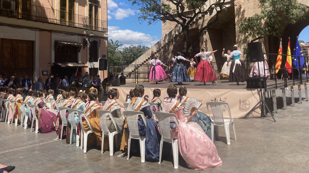 A row of women in traditional Valencian dress watching traditional dancing on a stage in front of Torres Serranos.