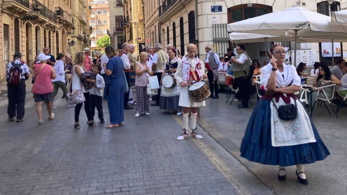 A woman in traditional Valencian dress talks on the phone as a group of tourists gathers nearby in the historic city center of Valencia