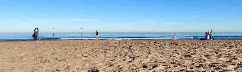 Sandy beach in Valencia, Spain with pedestrians walking along the blue horizon