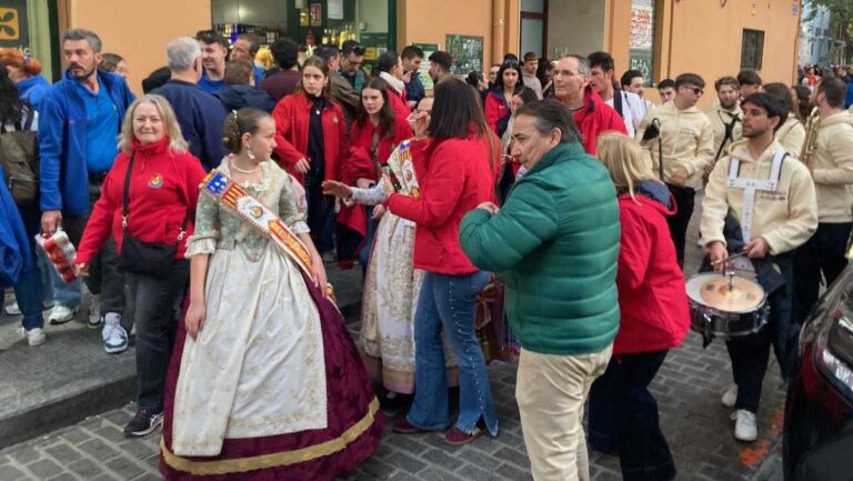 A young girl in traditional Valencia dress is escorted down a street with a marching band