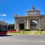 A red bus circling a roundabout with an arched monument in downtown Valencia, Spain