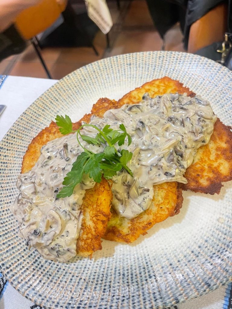 A plate of potato panckes covered in a creamy mushroom sauce