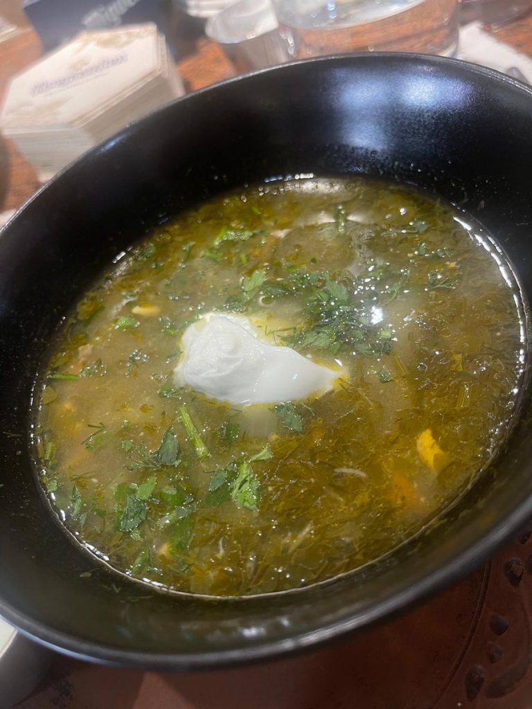 A bowl of green borscht soup with a dollop of white sour cream inside