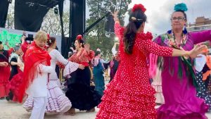 Women in bright flamenco style dresses dance at an open air festival