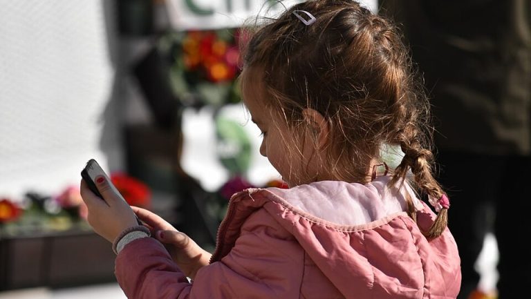 Young girl in pink jacket using a smart phone in public