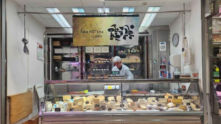 The owner of Formatges cheese store in Mercado Russafa behind a glass display of cheese