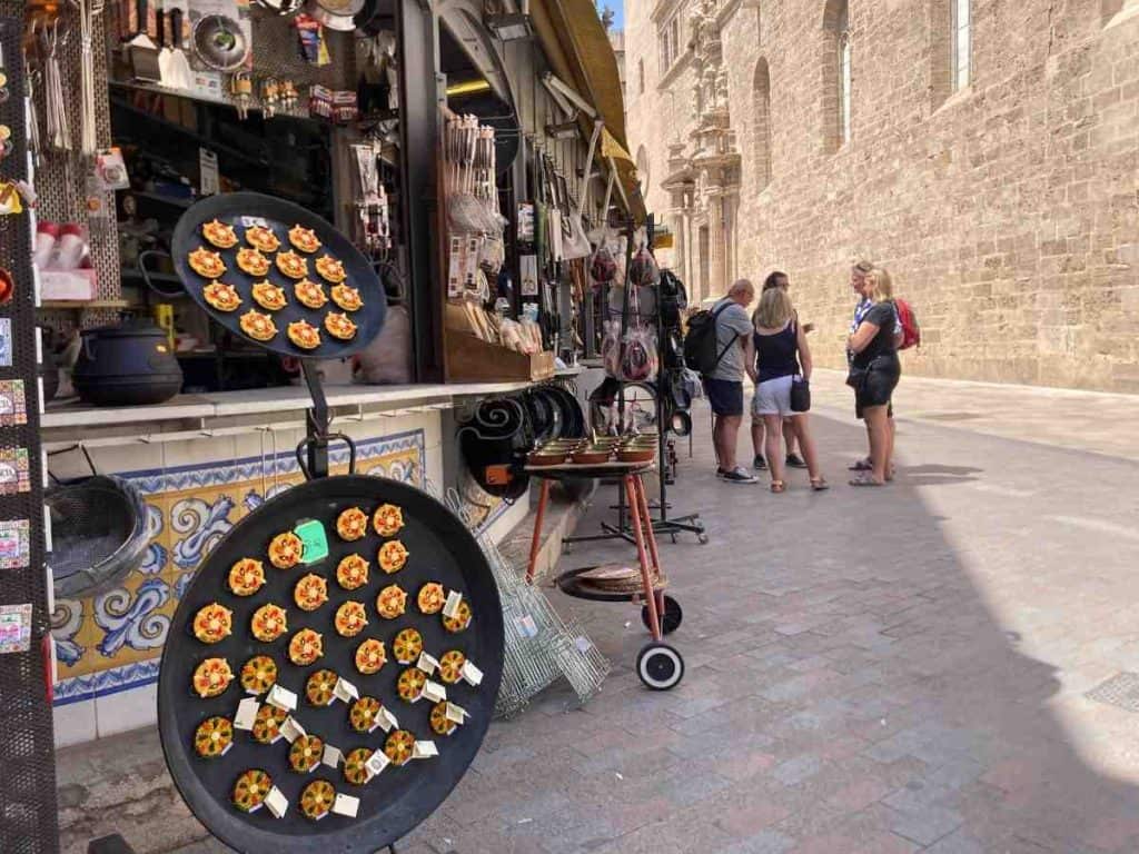 A group of tourists stand outside Valencia's Mercado Central, next to a stall selling paella pans.