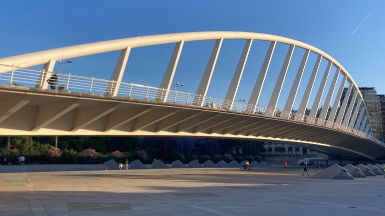 A view of the modern steel arc of the bridge Pont de l'Exposicio crossing over the Turia park on a sunny day with blue skies