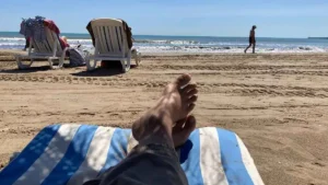 2 Beach chairs set up near the shore at Valencia's Malvarrosa Beach, with a pair of feet propped up in the foreground on a blue and white beach towel