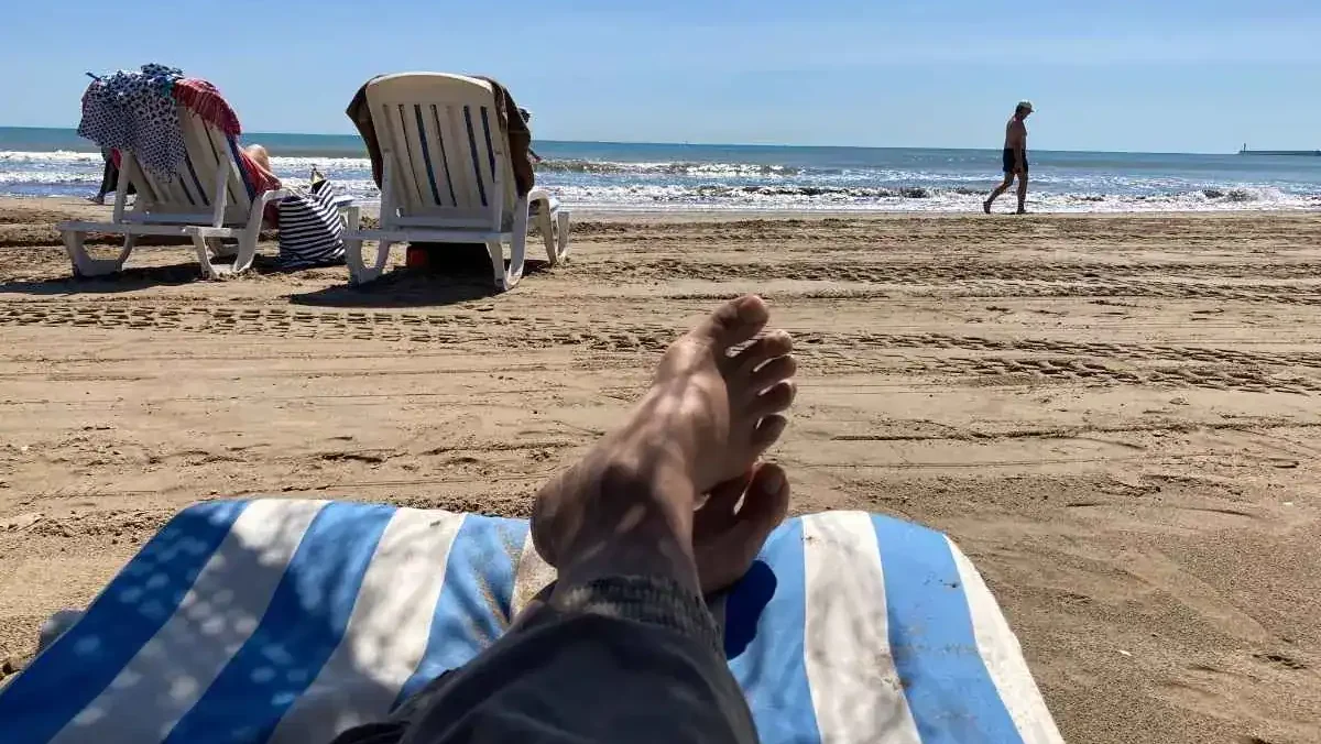 2 Beach chairs set up near the shore at Valencia's Malvarrosa Beach, with a pair of feet propped up in the foreground on a blue and white beach towel