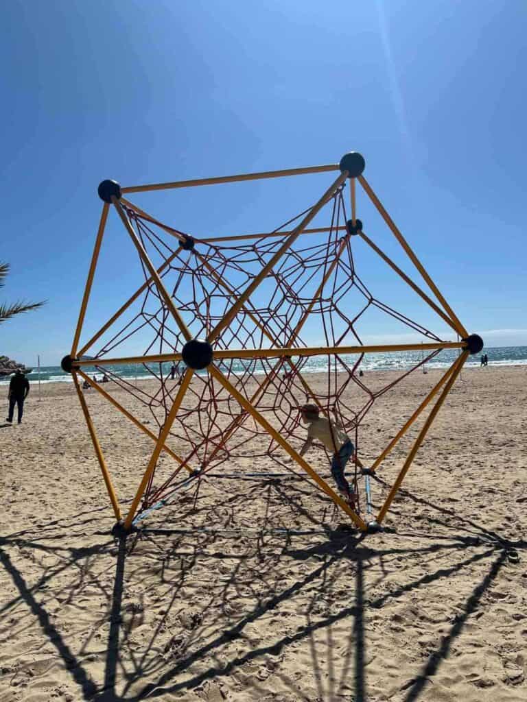 Children playing in the sunshine on a geometric spider web playground at Valencia beach.