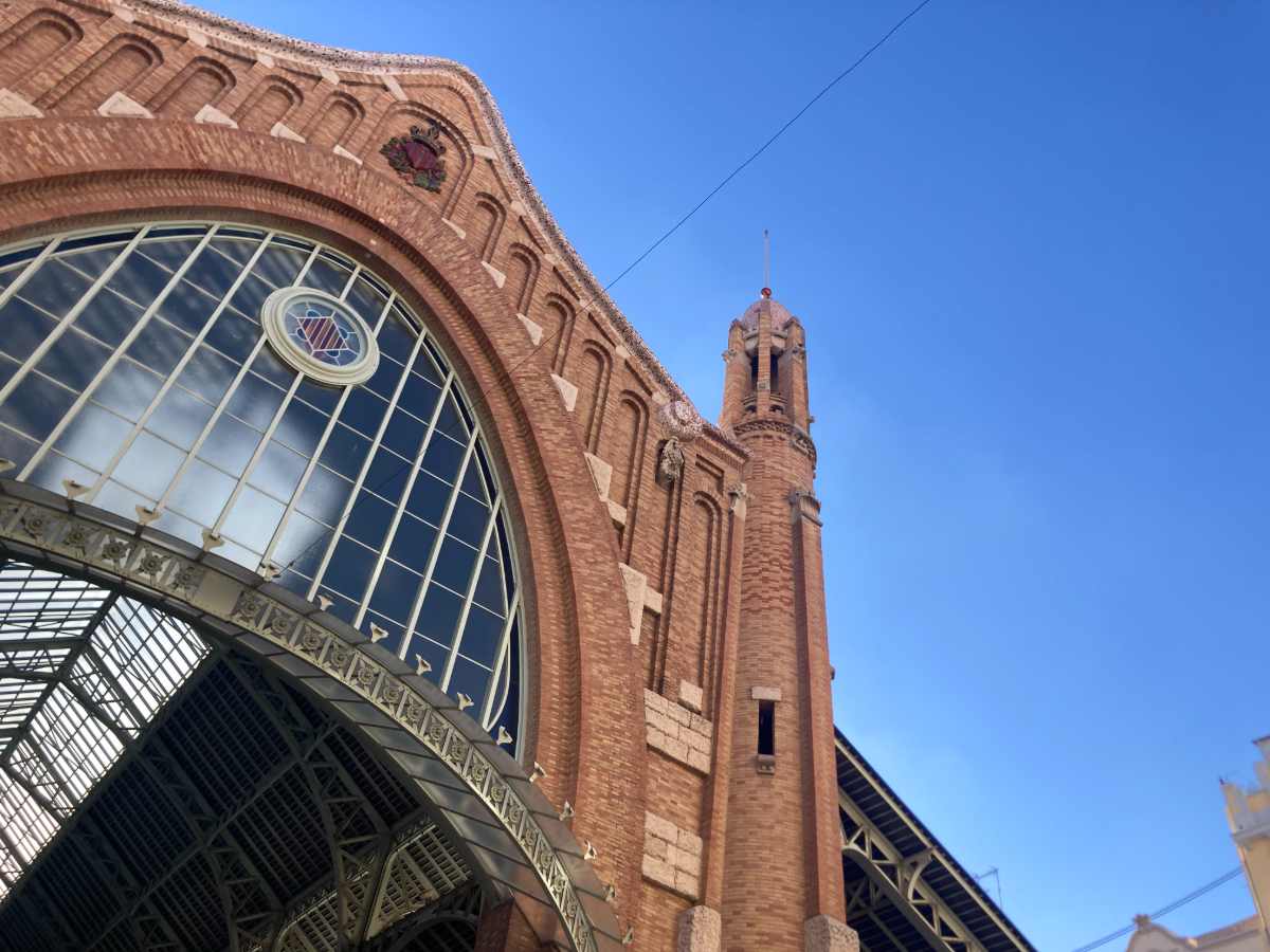 The brick and mosaic facade of Mercado Colon in Valencia against a cloudless blue sky